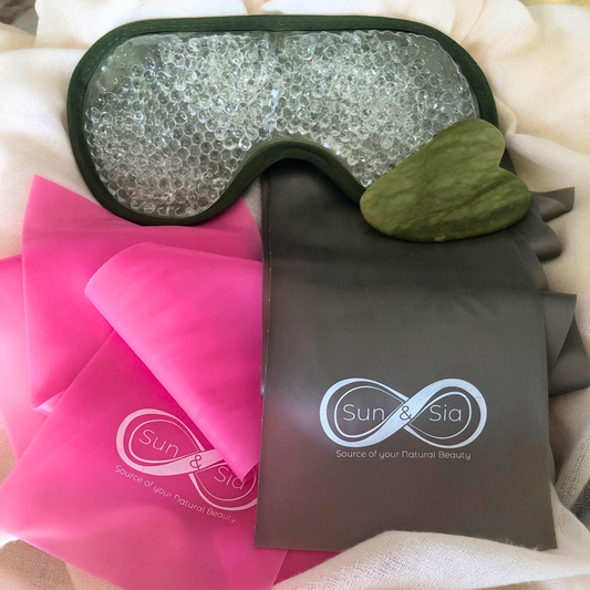 Sun & Sia wellness bundle flat lay with gel eye mask, jade gua sha stone, and pink and grey resistance bands on white linen