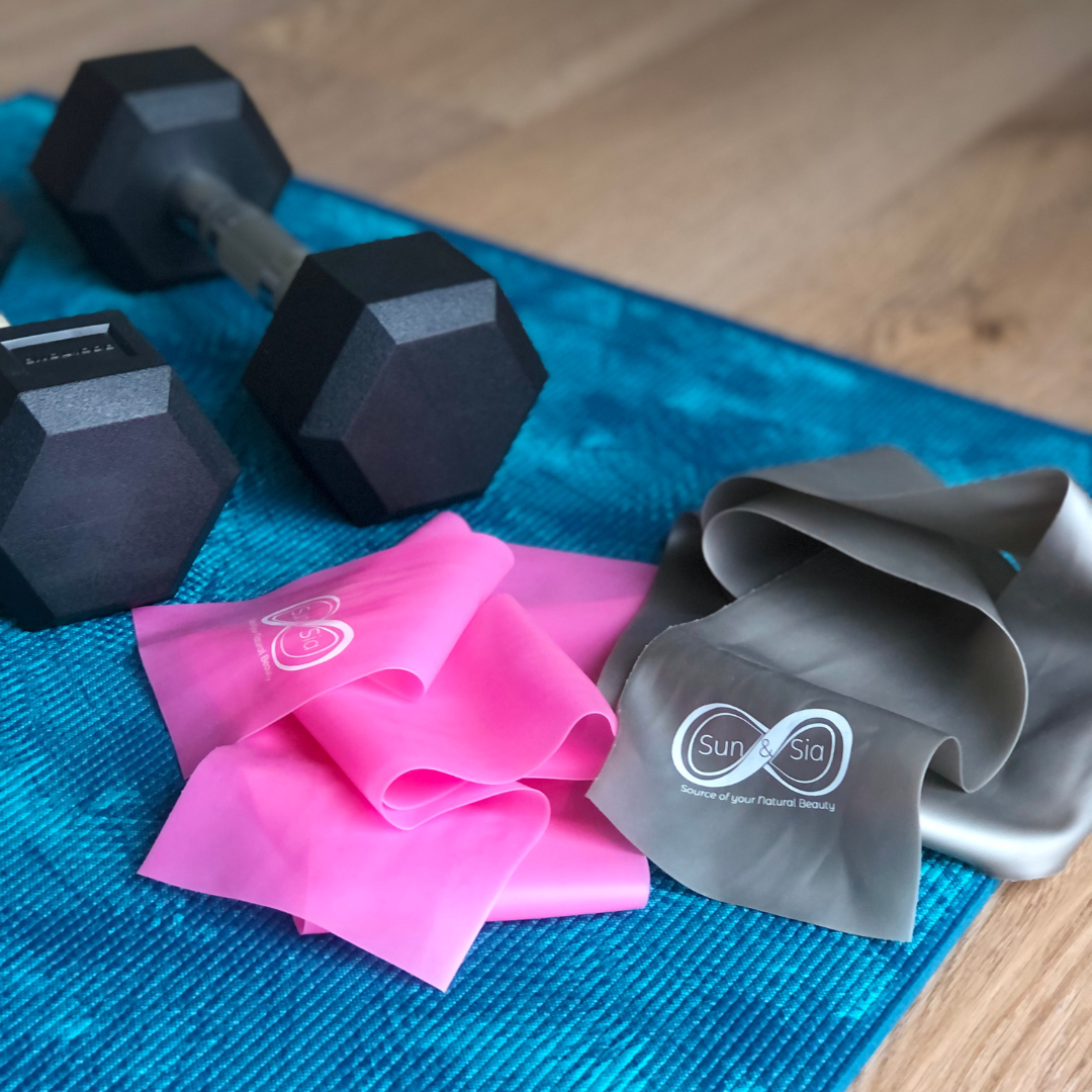 Sun & Sia pink and grey resistance bands on blue yoga mat next to black hex dumbbells